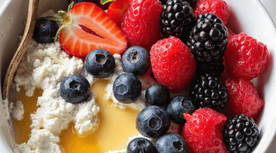 A protein-packed cottage cheese berry bowl topped with fresh strawberries, blueberries, raspberries, blackberries, and a drizzle of honey, served in a white bowl.