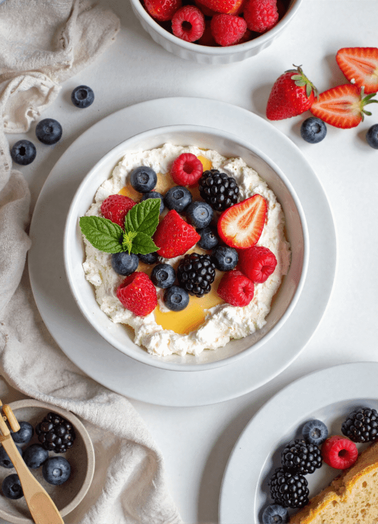 A healthy breakfast bowl filled with cottage cheese, blueberries, strawberries, blackberries, and raspberries, topped with honey and fresh mint.