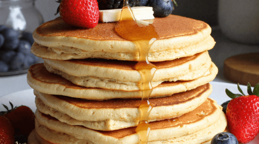 Stack of fluffy protein pancakes topped with fresh berries and banana slices, drizzled with maple syrup