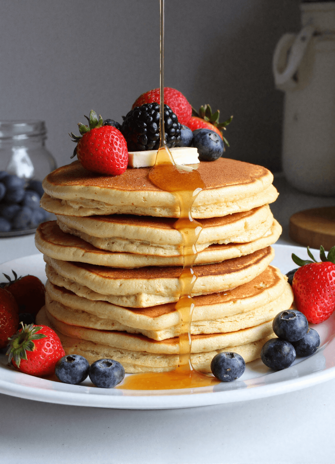 Stack of fluffy protein pancakes topped with fresh berries and banana slices, drizzled with maple syrup