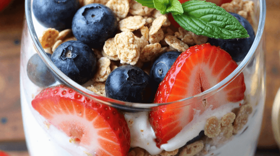 Layered high protein Greek yogurt parfait with blueberries, strawberries, granola, and honey drizzle in a tall glass