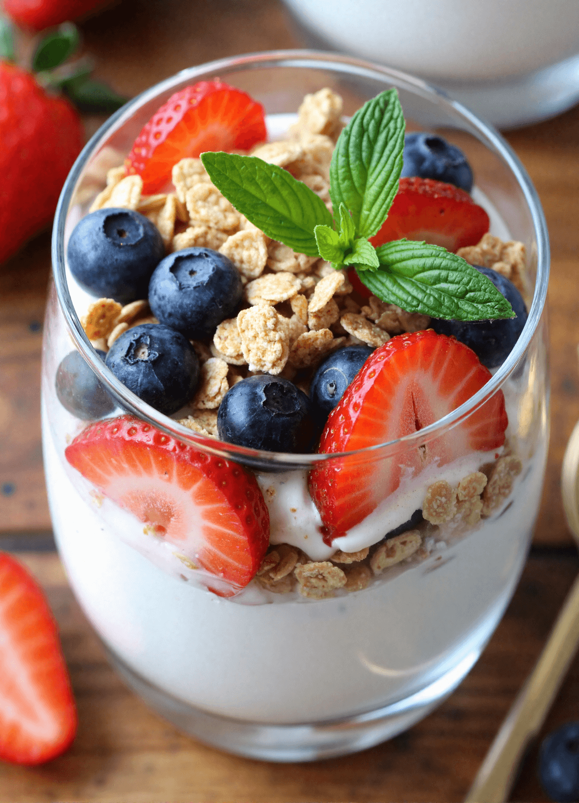 Layered high protein Greek yogurt parfait with blueberries, strawberries, granola, and honey drizzle in a tall glass