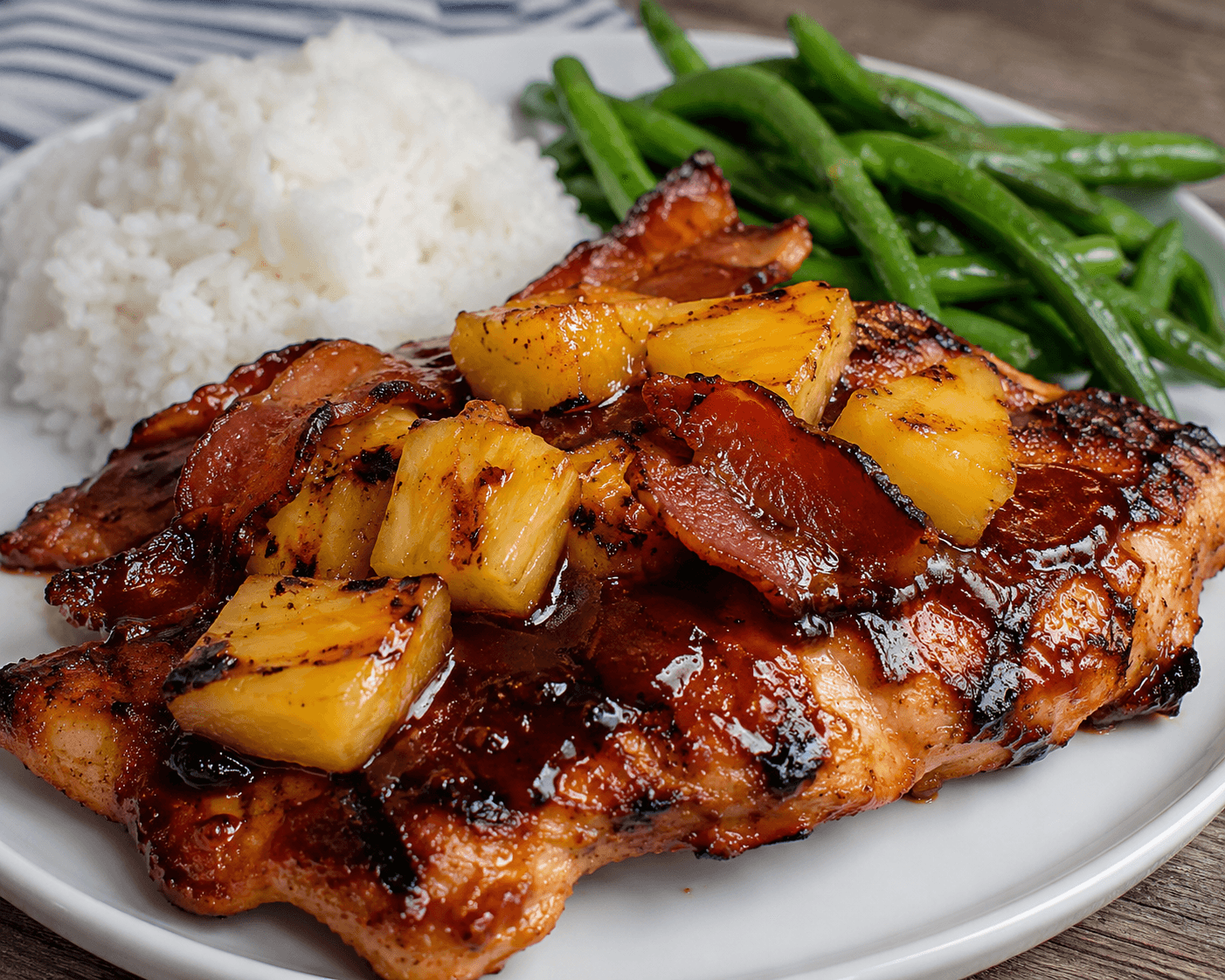 Grilled pineapple BBQ chicken topped with crispy beef bacon and caramelized pineapple chunks, served with rice and green beans for a quick sweet smoky dinner.