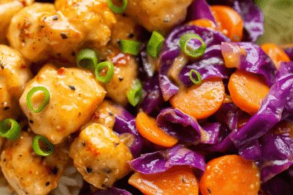 A close-up of juicy Bang Bang Chicken Bites coated in spicy-sweet sauce, surrounded by sautéed carrots and purple cabbage on a bed of white rice.