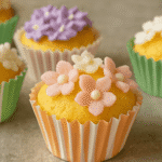 A top view of freshly baked Hokkaido chiffon cupcakes decorated with pastel flower icing, placed in colorful cupcake liners on a black ceramic plate.