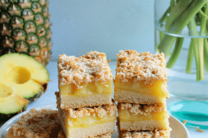 Tropical pineapple coconut bars stacked on a ceramic plate with pineapple slices and toasted coconut – recipe by readyprepmeals