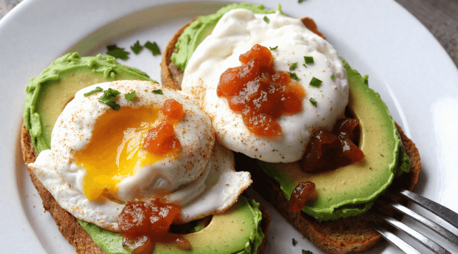 Avocado toast with poached eggs and bacon jam served on a white plate over a rustic wooden table – a perfect Father's Day breakfast idea.