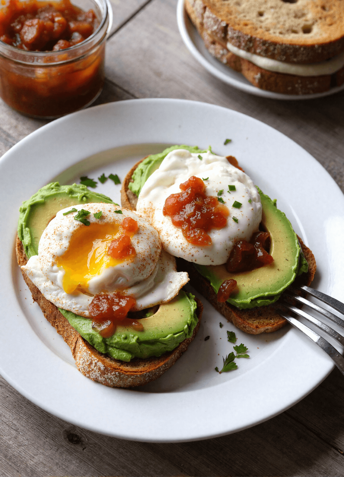 Avocado toast with poached eggs and bacon jam served on a white plate over a rustic wooden table – a perfect Father's Day breakfast idea.