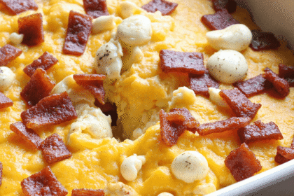 Freshly baked bacon cheddar breakfast casserole in a white ceramic baking dish, featuring golden melted cheese, crispy bacon, and rustic cubed bread