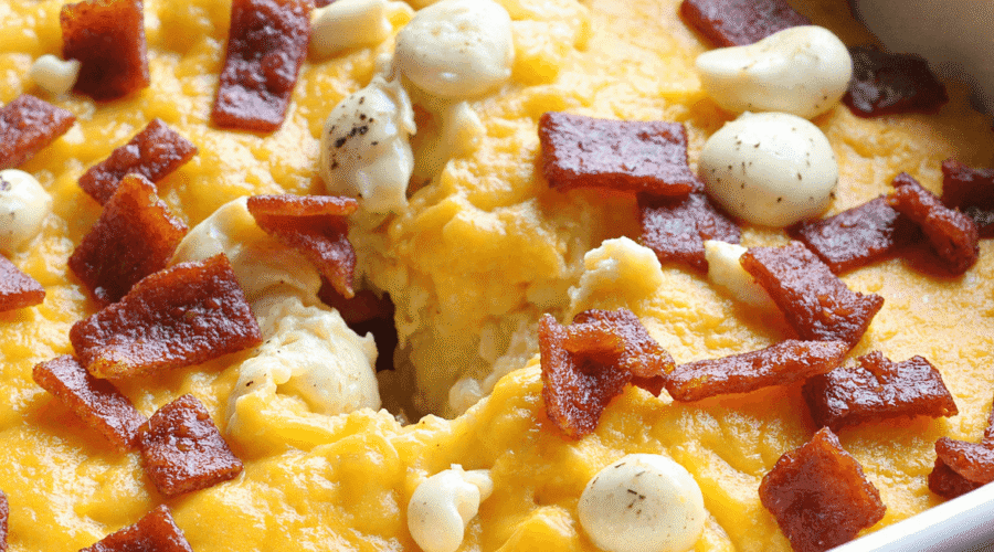 Freshly baked bacon cheddar breakfast casserole in a white ceramic baking dish, featuring golden melted cheese, crispy bacon, and rustic cubed bread