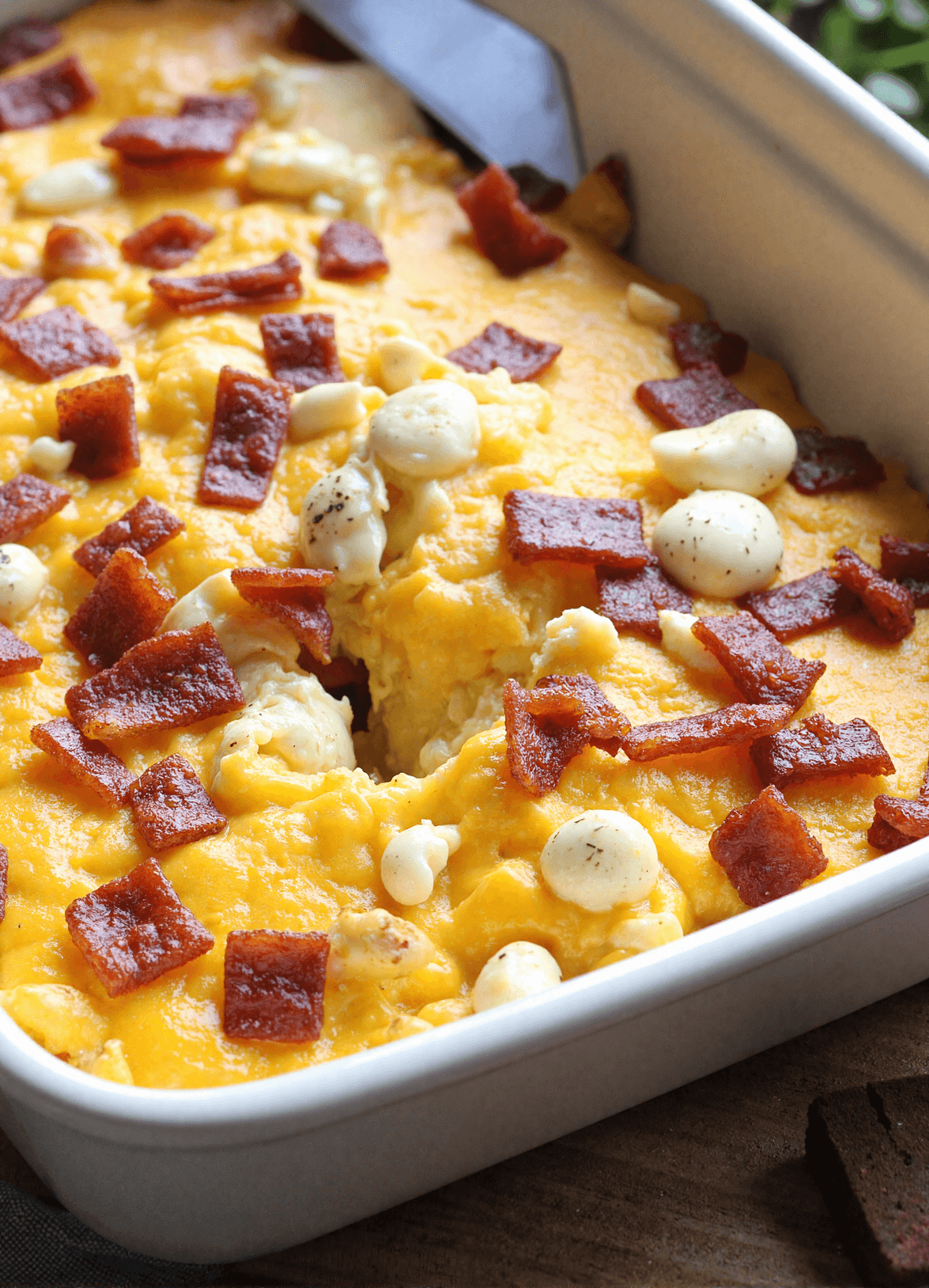 Freshly baked bacon cheddar breakfast casserole in a white ceramic baking dish, featuring golden melted cheese, crispy bacon, and rustic cubed bread