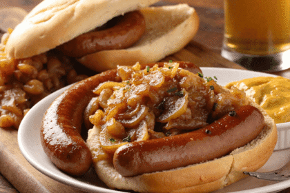 Beer-braised bratwursts served in a rustic dish, topped with caramelized lentils and onions, with mustard and crusty bread on the side.