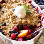 Summer fruit crumble with peaches and berries in a rustic baking dish, topped with golden crumble and a scoop of vanilla ice cream