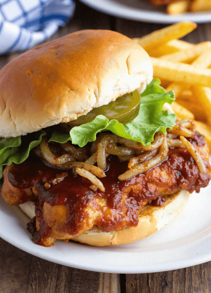 Bourbon BBQ chicken sandwich with grilled chicken, barbecue glaze, lettuce, pickles, and crispy onions in a brioche bun, plated with fries for Father’s Day meal.