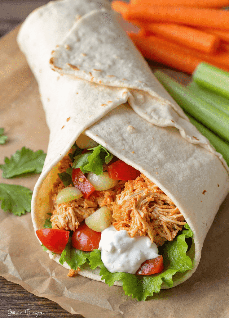 Buffalo Chicken Wrap with shredded chicken, lettuce, tomatoes, pickles, and blue cheese dressing in a soft tortilla, served with carrot and celery sticks