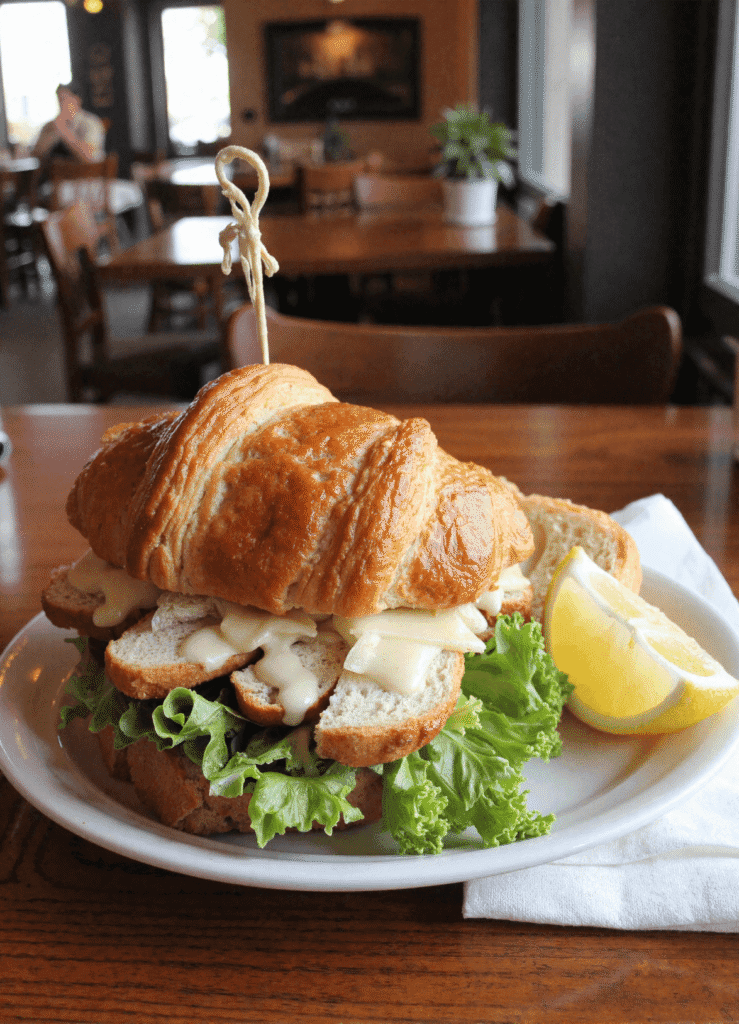 Croissant sandwich filled with sliced chicken, romaine lettuce, melted cheese, and Caesar dressing on a white plate