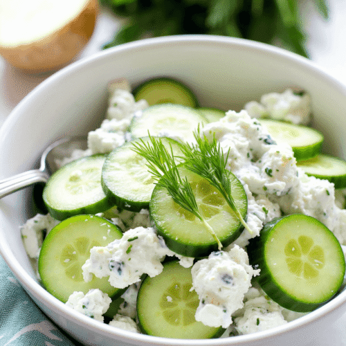 Chilled cucumber yogurt salad served in a white ceramic bowl, garnished with fresh dill and a drizzle of olive oil