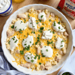 A homemade creamy chicken casserole in a white baking dish, topped with golden breadcrumbs, surrounded by fresh ingredients like sour cream, broth, and shredded cheese, set on a wooden countertop in a bright kitchen.
