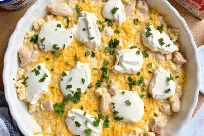 A homemade creamy chicken casserole in a white baking dish, topped with golden breadcrumbs, surrounded by fresh ingredients like sour cream, broth, and shredded cheese, set on a wooden countertop in a bright kitchen.