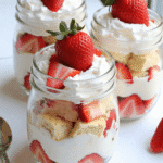Individual no-bake strawberry shortcake trifles layered with pound cake, whipped cream, and fresh strawberries in clear glass jars