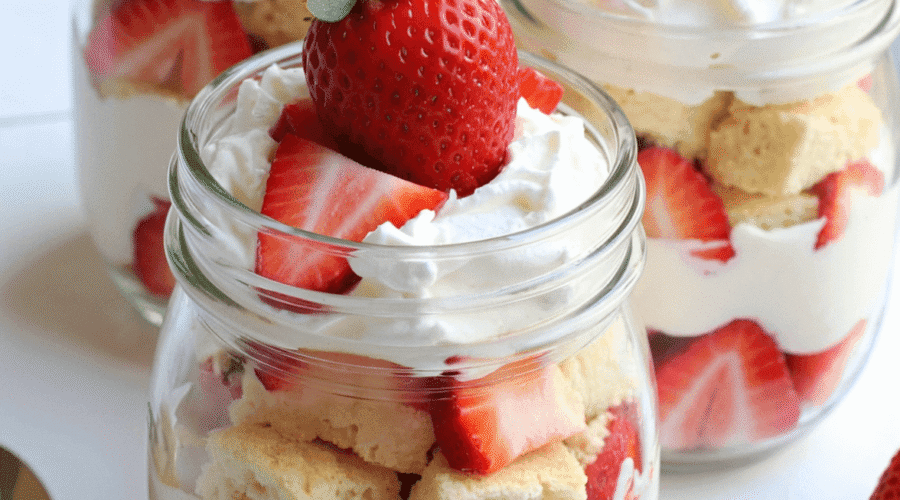 Individual no-bake strawberry shortcake trifles layered with pound cake, whipped cream, and fresh strawberries in clear glass jars
