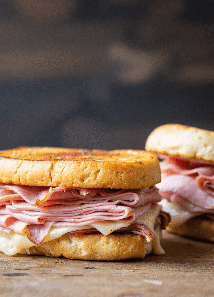 Grilled Cuban Sandwiches stacked and sliced, filled with layers of ham, roast pork, Swiss cheese, and pickles on buttery toasted bread