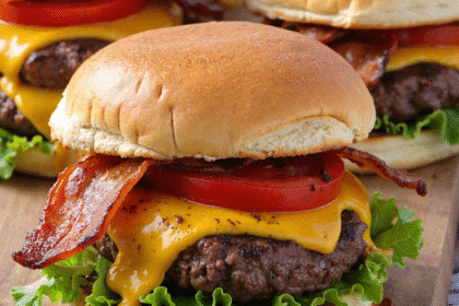 Close-up of loaded cheeseburger sliders with cheddar, crispy bacon, lettuce, and tomato on toasted buns.