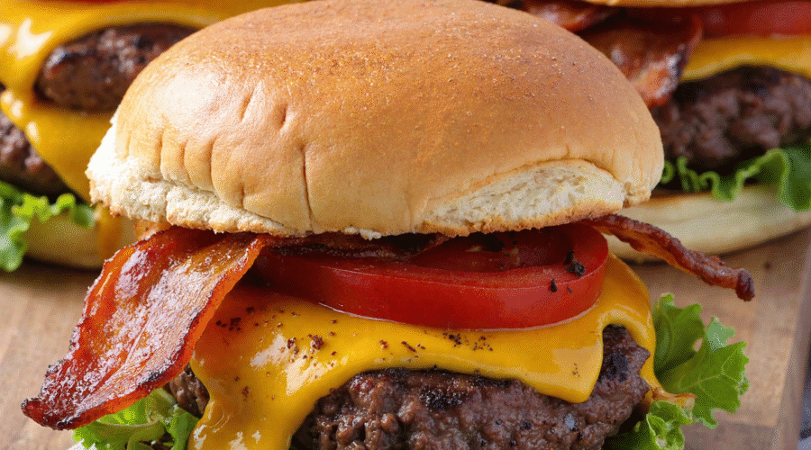 Close-up of loaded cheeseburger sliders with cheddar, crispy bacon, lettuce, and tomato on toasted buns.