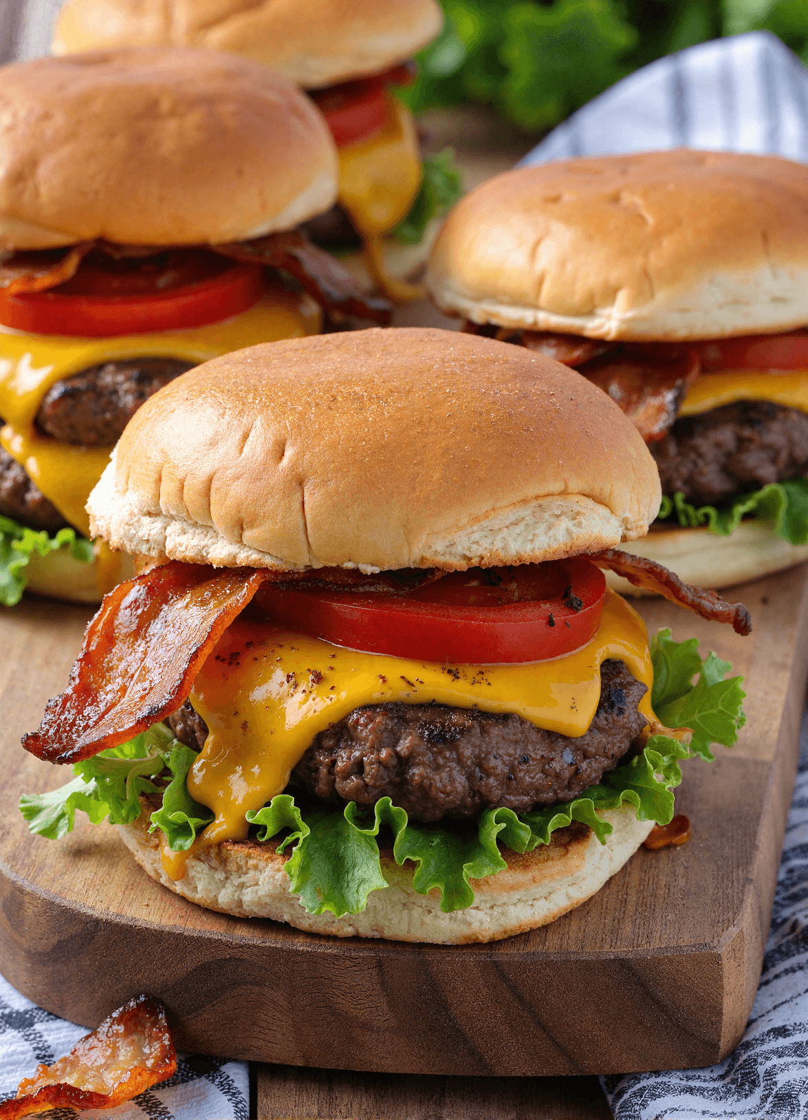 Close-up of loaded cheeseburger sliders with cheddar, crispy bacon, lettuce, and tomato on toasted buns.