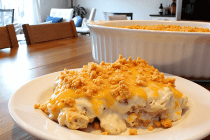 A serving of million dollar chicken casserole on a white plate, featuring creamy chicken filling topped with golden Ritz cracker crumbs, set on a wooden table in a bright, modern kitchen.