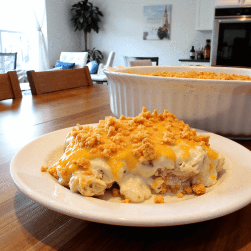 A serving of million dollar chicken casserole on a white plate, featuring creamy chicken filling topped with golden Ritz cracker crumbs, set on a wooden table in a bright, modern kitchen.