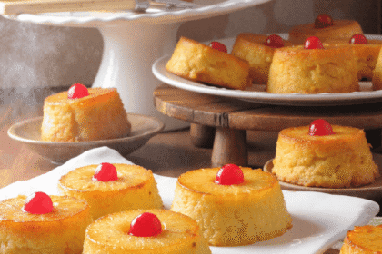 Mini pineapple upside down cakes topped with cherries on a wooden board, golden and caramelized, with pineapple rings and melted brown sugar glaze