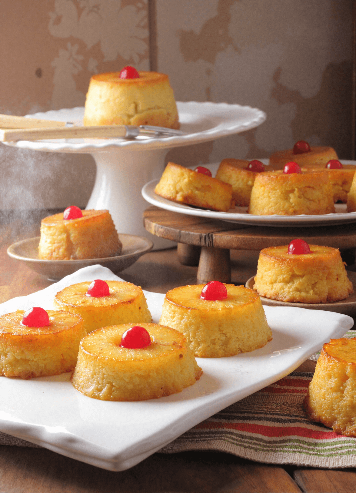 Mini pineapple upside down cakes topped with cherries on a wooden board, golden and caramelized, with pineapple rings and melted brown sugar glaze