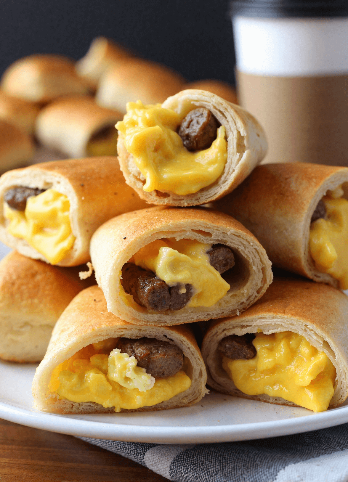 Golden sausage, egg, and cheese breakfast roll-ups sliced open on a wooden board with melted cheddar and savory sausage inside