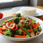 Colorful stir-fried vegetables including broccoli, bell peppers, snap peas, carrots, and mushrooms in a garlic soy sauce, garnished with sesame seeds. Photo by @readyprepmeals.