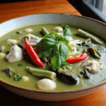 Thai green curry with chicken, bamboo shoots, and Thai eggplant in a creamy coconut sauce, garnished with red chili slices and fresh basil leaves. Photo by Sam @readyprepmeals.