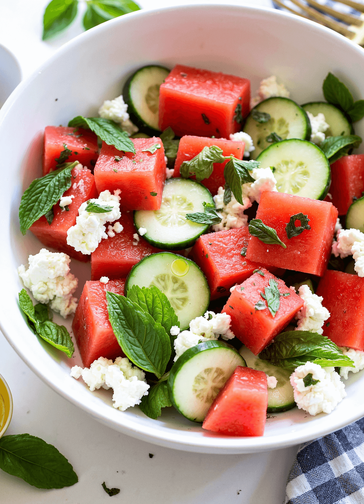 Watermelon feta salad with mint and cucumber served in a white ceramic bowl on a rustic wood table, garnished with fresh herbs and lime wedges