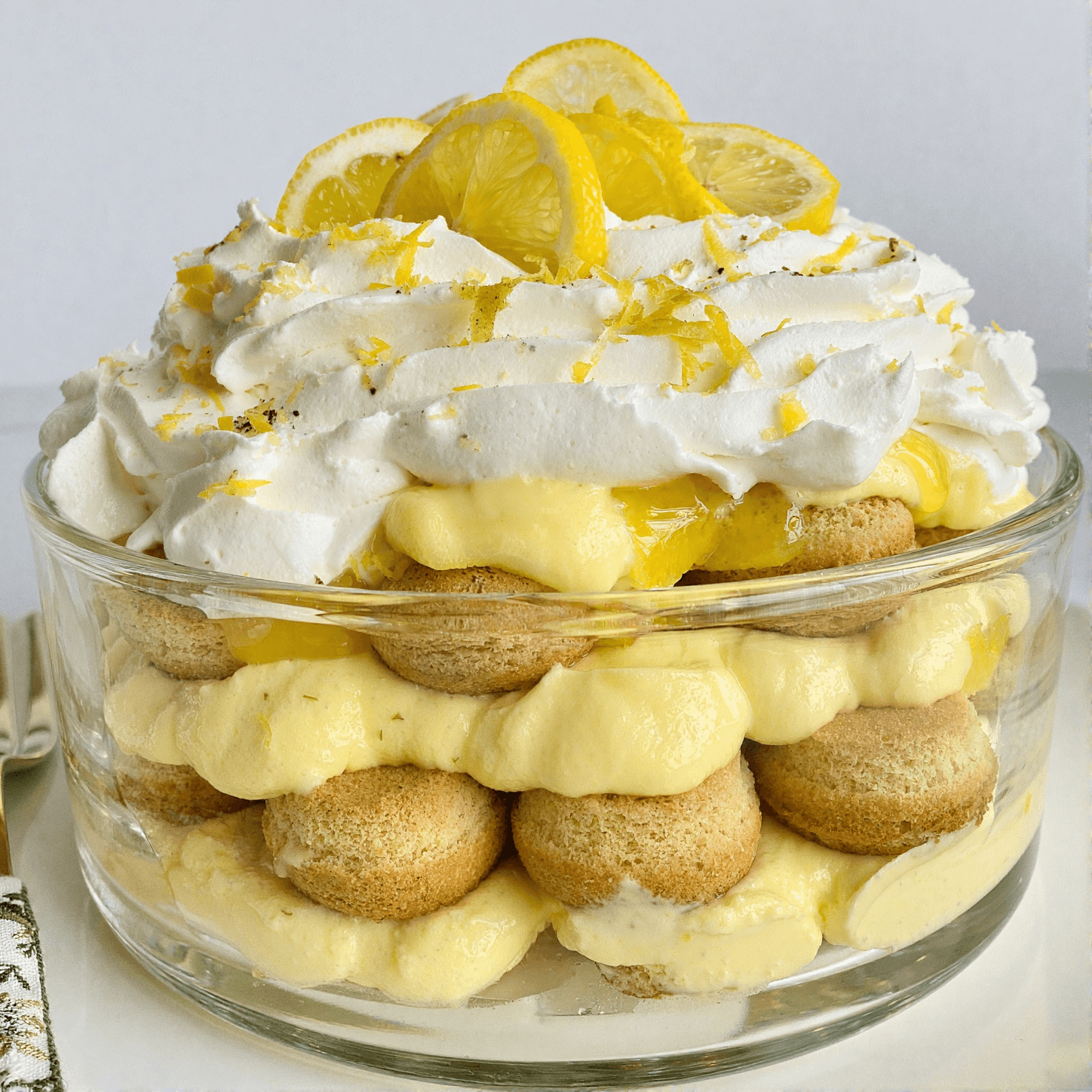 Front view of lemon tiramisu layered with mascarpone cream, ladyfingers, whipped topping, and fresh lemon slices
