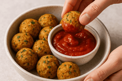 Hands dipping a golden-brown tofu meatball into marinara sauce, served in a rustic bowl filled with parsley-garnished meatballs, photographed by Sam from ReadyPrepMeals.