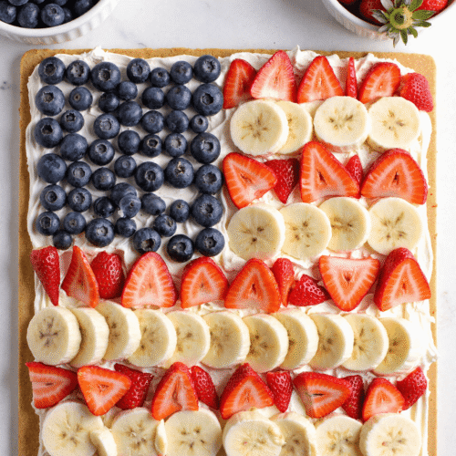 Close-up of American Flag Fruit Pizza with sugar cookie crust, whipped cream cheese frosting, and rows of strawberries, blueberries, and bananas in a patriotic red, white, and blue pattern.