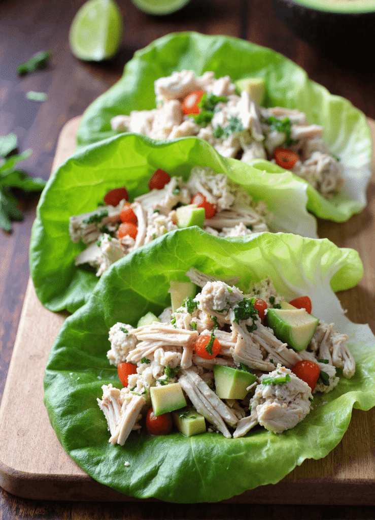 avocado chicken salad lettuce wraps with shredded chicken, diced avocado, cherry tomatoes, and fresh herbs served on butter lettuce leaves