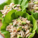 keto chicken avocado lettuce wraps with shredded chicken, avocado cubes, and herbs in butter lettuce leaves on a wooden board