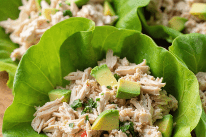 keto chicken avocado lettuce wraps with shredded chicken, avocado cubes, and herbs in butter lettuce leaves on a wooden board