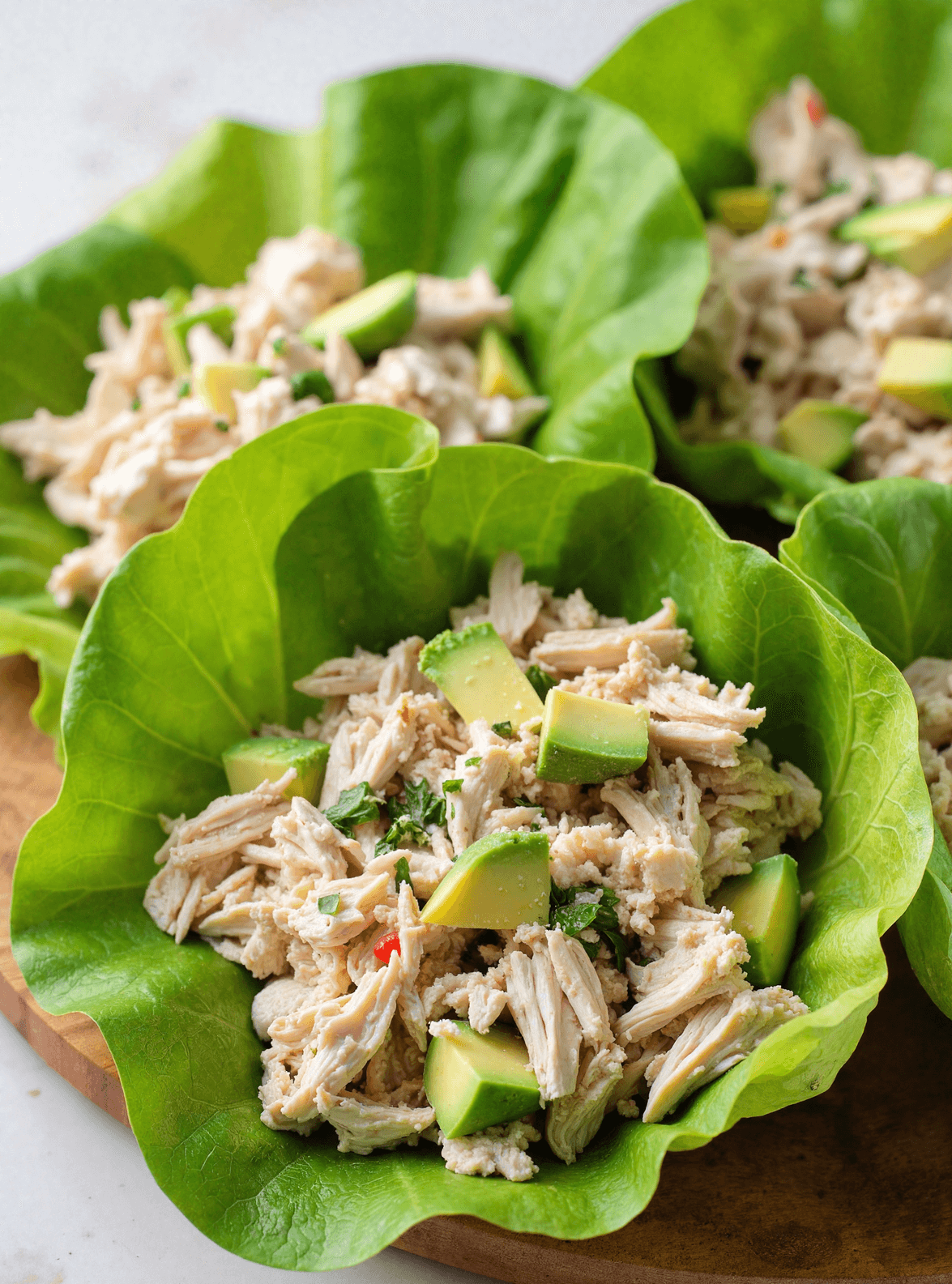 keto chicken avocado lettuce wraps with shredded chicken, avocado cubes, and herbs in butter lettuce leaves on a wooden board