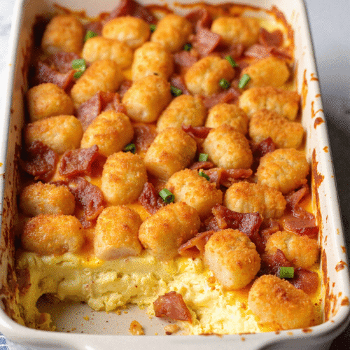 Golden brown bacon, egg, and tater tot casserole baked in a white dish with a crispy top and melted cheddar cheese.