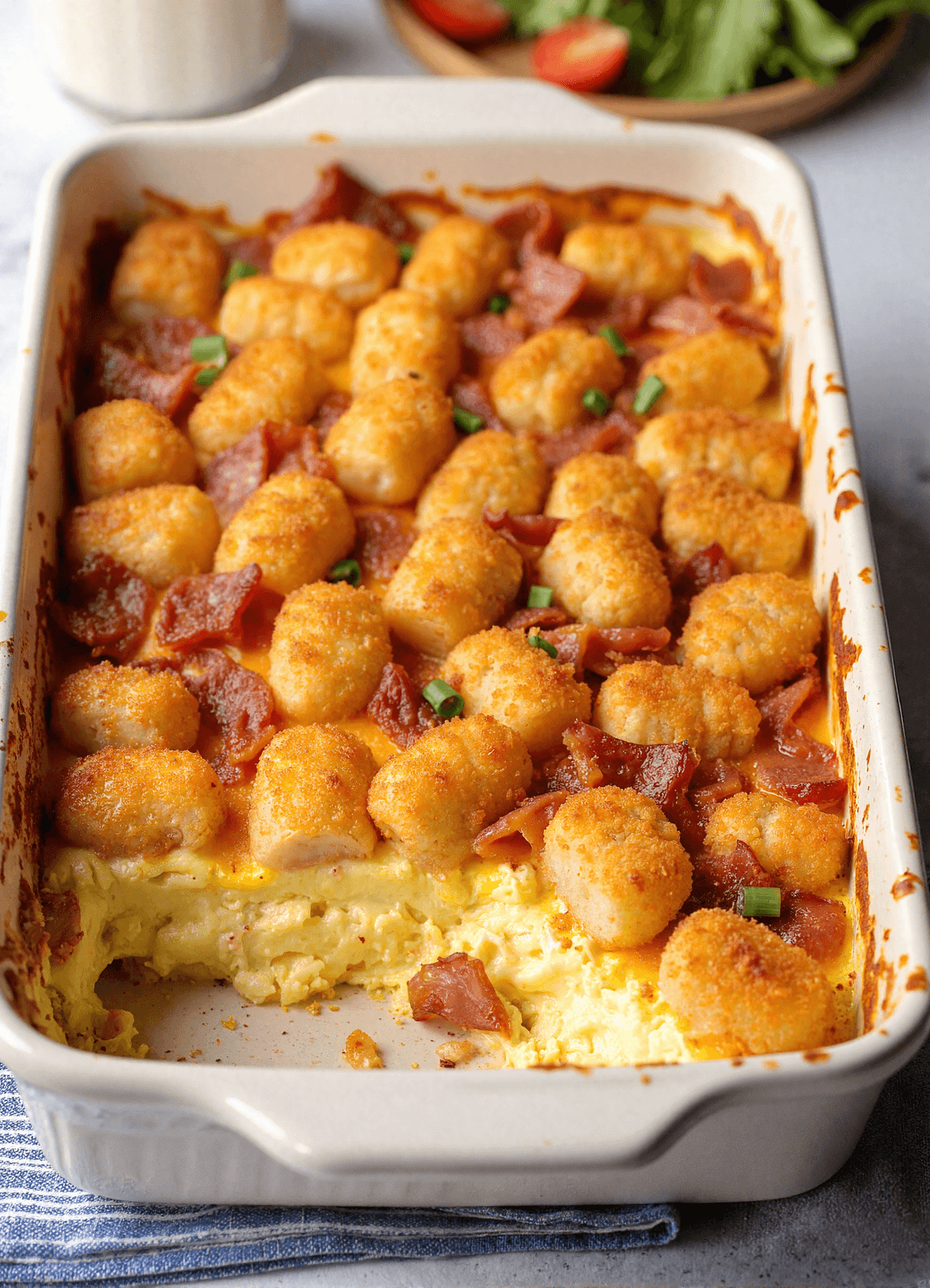 Golden brown bacon, egg, and tater tot casserole baked in a white dish with a crispy top and melted cheddar cheese.