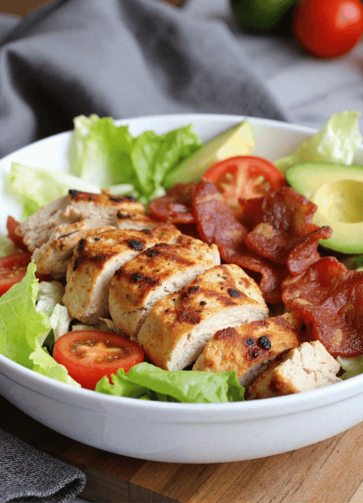 Grilled chicken breast with crispy bacon, romaine lettuce, cherry tomatoes, and avocado in a protein-packed BLT chicken salad bowl