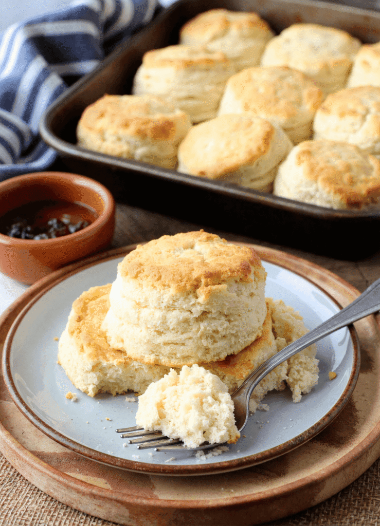 Close-up of breakfast butter swim biscuits on a plate with a fork and jam in the background, showcasing fluffy texture.