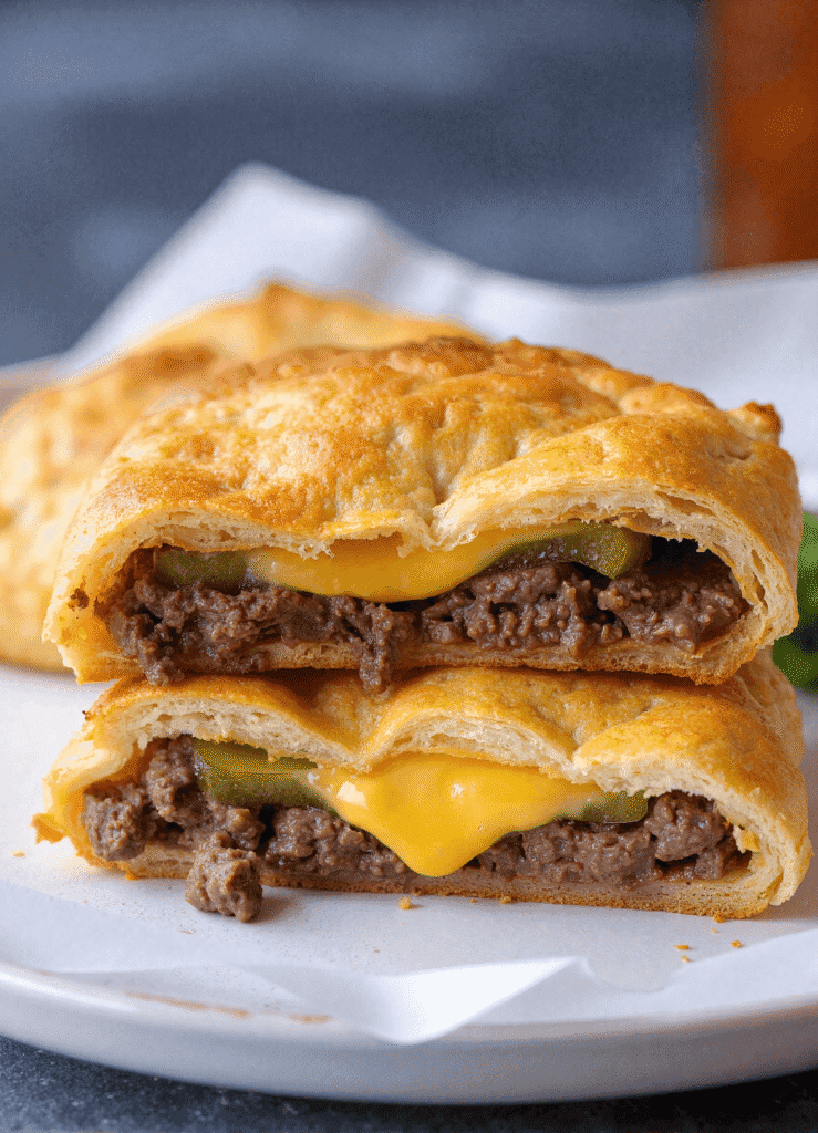 Mini round cheeseburger pocket sliced in half showing juicy ground beef patty, melted cheese, and sliced pickles inside a soft golden crust.