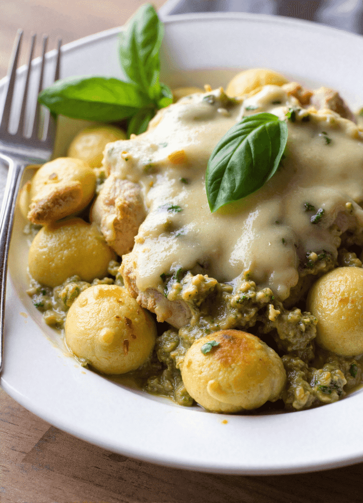 creamy pesto chicken and gnocchi bake with crispy breaded chicken, rich pesto sauce, melted cheese, and tender gnocchi, garnished with fresh basil